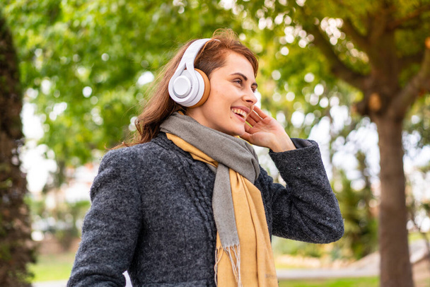 Brunette nainen kuuntelee musiikkia kuulokkeet ulkona pitää keskustelun matkapuhelimen kanssa - Valokuva, kuva