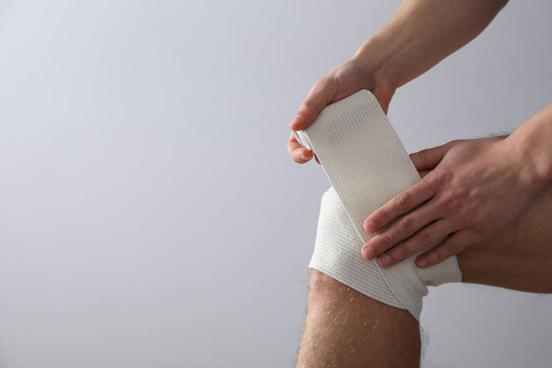 Έννοια της βοήθειας κατά τη διάρκεια ενός τραυματισμού, ο άνθρωπος τυλίγοντας το γόνατο σε επίδεσμο σε λευκό φόντο - Φωτογραφία, εικόνα