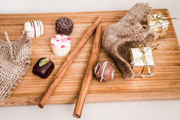 Chocolade mini pralines versierd met kaneelstokje en kleine pakjes in gouden kleur op tafel. - Foto, afbeelding