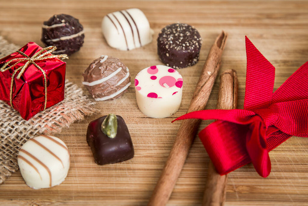 Chocolate pralineia doces doces de Natal. Pacotes pequenos com decoração de férias, fita vermelha em madeira. - Foto, Imagem