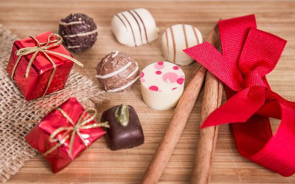 Pralines de chocolate com decoração de fita vermelha, pau de canela e pequenos pacotes. - Foto, Imagem