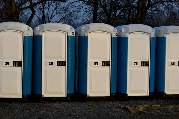 toilette mobile in plastica bianca blu che giace sul suo lato. Rovinato grazie a atti vandalici, ubriachi, rivolte di teppisti. piazza per parco, WC chimico accessibile fuori servizio, albero, fila, parco - Foto, immagini
