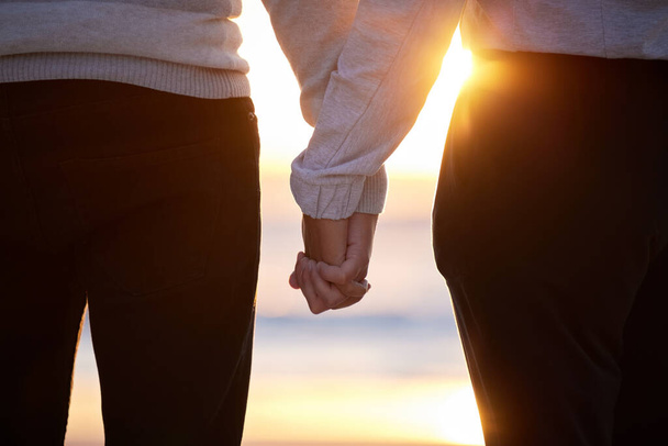 Beach, couple and holding hands at sunset for love and trust or commitment and support on vacation. Hand of man and woman together on holiday at sea to relax, travel and connect in nature with care. - Photo, Image