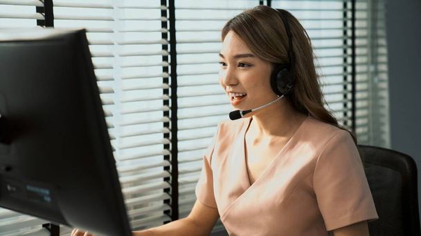 Competent female operator working on computer and while talking with clients. Concept relevant to both call centers and customer service offices. - Foto, imagen