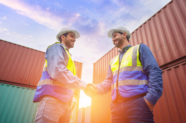 Two engineer container cargo wearing white hardhat and safety vests in successful handshake together at container yard. success in logistics business import export industry - Photo, Image