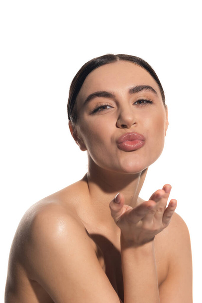 fröhliche junge Frau mit natürlichem Make-up schmollenden Lippen beim Senden Luftkuss isoliert auf weiß - Foto, Bild