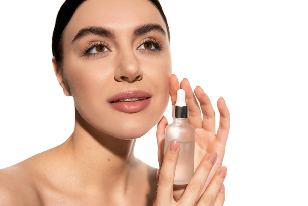 dreamy woman with bare shoulders holding bottle with moisturizing serum isolated on white  - Fotografie, Obrázek
