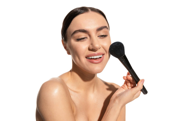 jovem alegre com ombros nus segurando escova de pó macio perto da bochecha isolada no branco  - Foto, Imagem