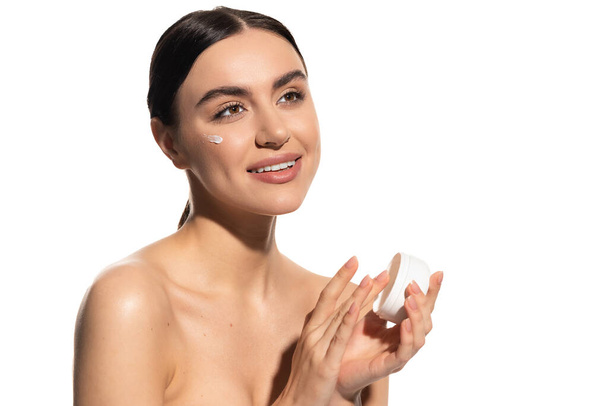happy young woman with bare shoulders holding jar with moisturizing face cream isolated on white  - Foto, Bild