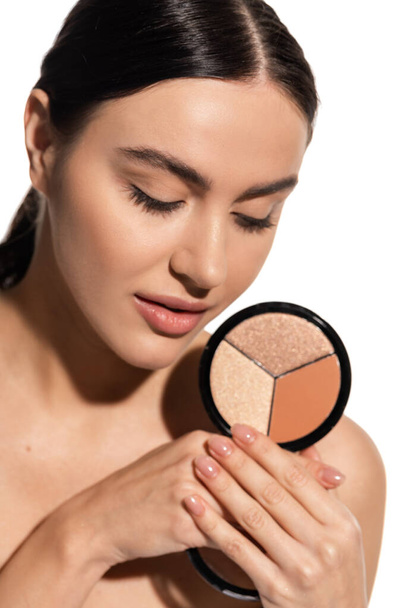 brunette young woman with bare shoulder holding bronzer and highlighter palette isolated on white  - Foto, imagen