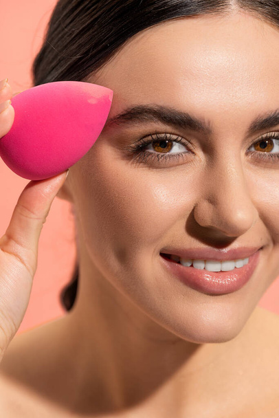 close-up uitzicht van gelukkig vrouw houden make-up spons geïsoleerd op roze  - Foto, afbeelding