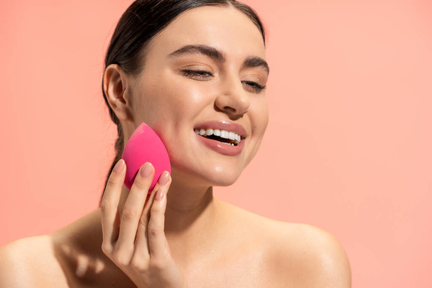 mujer feliz aplicación de la base de la cara con esponja de belleza aislado en rosa  - Foto, imagen