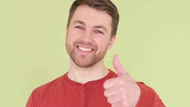Positive young man smiling at camera and giving thumbs up on yellow background. Winner. Success. Body language. - Séquence, vidéo