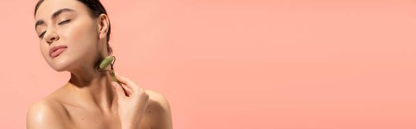 brunette young woman doing neck massage with jade roller isolated on pink, banner  - Photo, Image