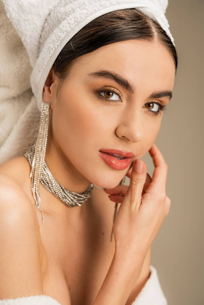 elegant young woman with makeup and jewelry looking at camera on grey  - Foto, Bild
