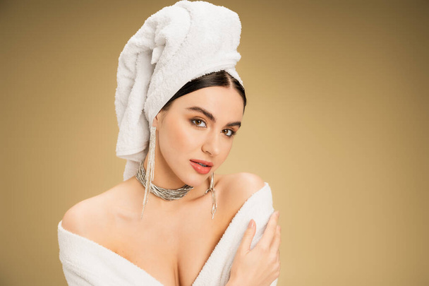 charming woman in jewelry with white towel on head looking at camera on beige background  - Foto, immagini
