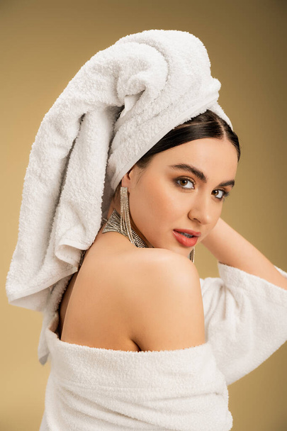 brunette woman with makeup and towel on head looking at camera on beige background  - Foto, Bild