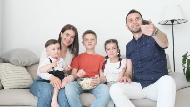 A family of five spends time together at home. They watch a movie, hug and eat popcorn. The family members look happy and satisfied with the time - Materiaali, video