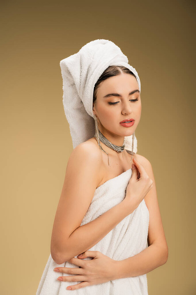 pretty woman in jewelry holding white towel on beige background  - 写真・画像