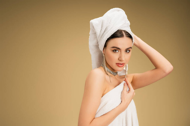 charming woman in luxurious jewelry adjusting white towel on beige background  - 写真・画像