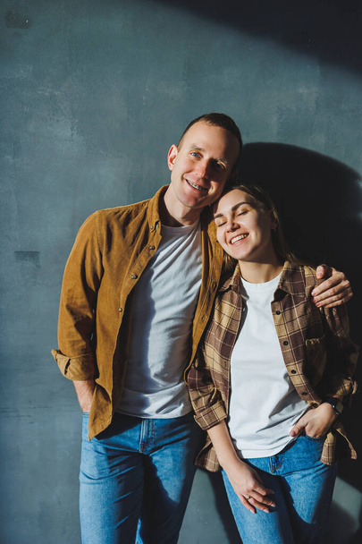 Happy couple in love dressed in shirts, standing on the background of gray wall, looking at empty space, isolated background of gray concrete wall. The concept of a happy couple in love. - Фото, изображение