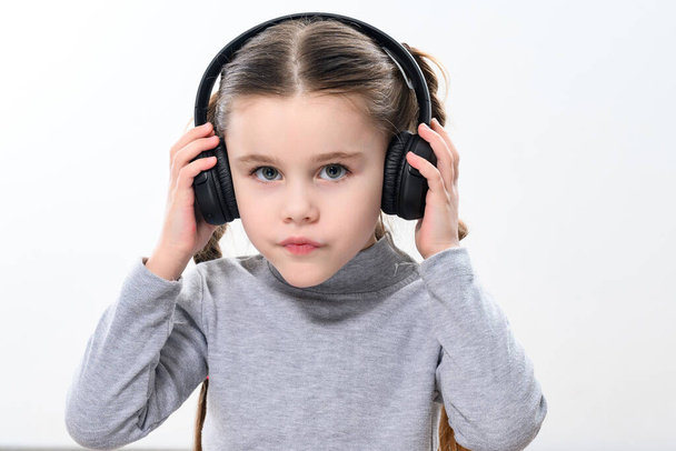 Ένα παιδί με ακουστικά σε λευκό φόντο, ένα χαρούμενο και όμορφο κορίτσι με ακουστικά, αντίγραφο χώρο σε λευκό φόντο. - Φωτογραφία, εικόνα