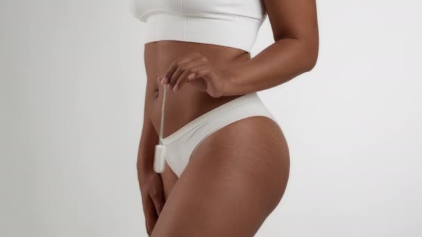 Secrets of female hygiene. Close up shot of unrecognizable black woman in underwear holding tampone, posing over white studio background, slow motion, free space - Záběry, video