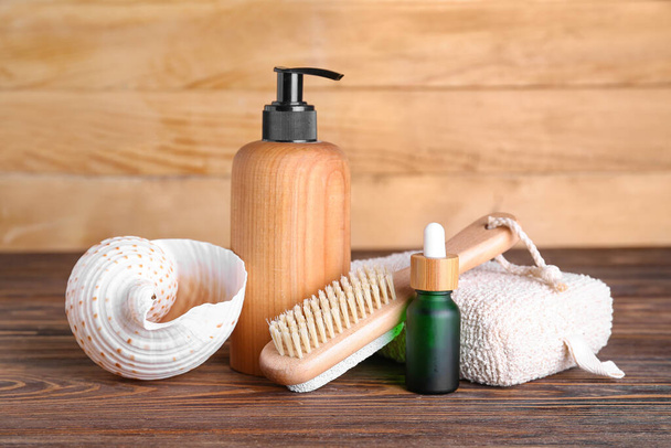 Бутылки косметических средств, губка для ванны, массажная щетка и раковина на деревянном фоне - Фото, изображение