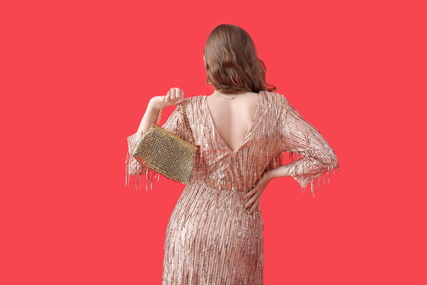 Young woman in shiny prom dress with bag on red background, back view - Foto, immagini