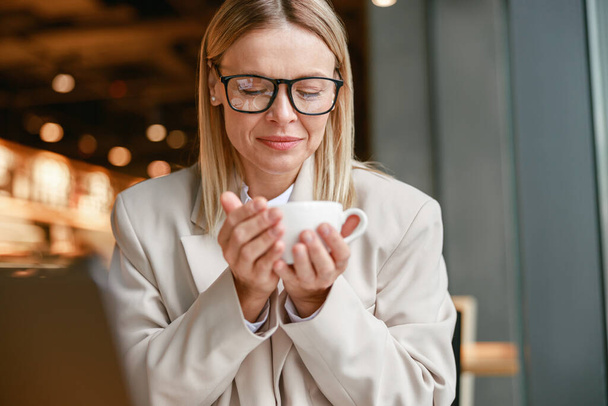 Mulher de negócios atraente segurando xícara de café enquanto sentado no café. Foto de alta qualidade - Foto, Imagem