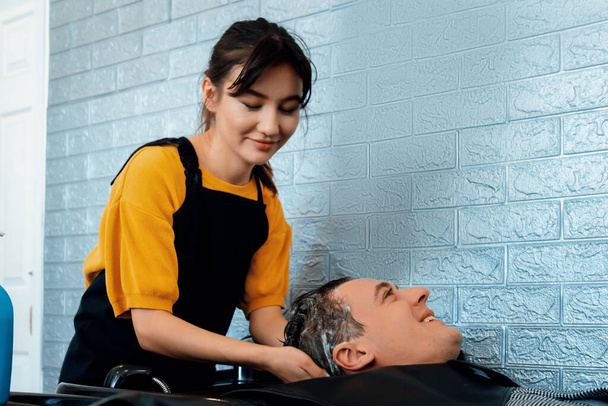 Caucasian man getting hair wash by professional hairdresser with shampoo feels relax and comfortable . Qualified hairdresser with her barbershop, salon providing haircare concept. - Photo, Image
