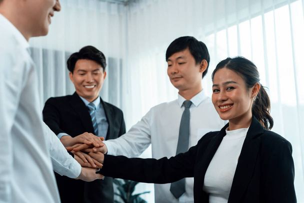 Closeup business team of suit-clad businessmen and women join hand stack together and form circle. Colleague collaborate and work together to promote harmony and teamwork concept in office workplace. - 写真・画像