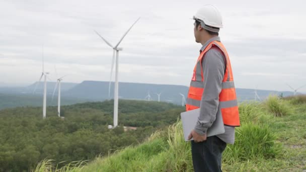 田舎の丘や山の上の風力発電所で働くエンジニア。再生可能エネルギー、持続可能なエネルギーの将来の生産のための進歩的な理想。風力タービンからの発電. - 映像、動画