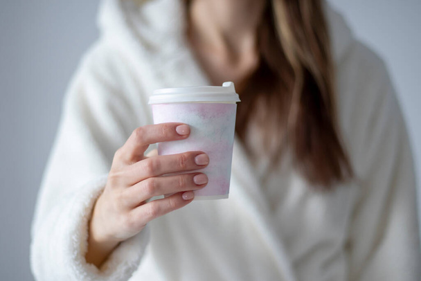 A woman holding a plastic coffee cup with a delicate watercolor drawing in her hand at home. - 写真・画像