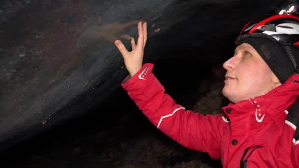 A guy enjoys the beauty in a mountain ice cave. It touches the centuries-old ice. Air bubbles and rocks froze in the ice wall. A lantern shines on walls of ice. An epic moment. There are big stones - Materiaali, video