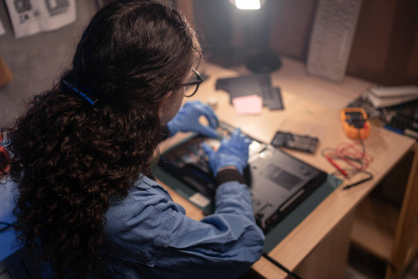 Técnico a reparar um portátil no antigo laboratório. Jovem mulher trabalhando, usando luvas em oficina retro. Conceito de computador de reparação, eletrônica, atualização, tecnologia. Espaço de cópia - Foto, Imagem