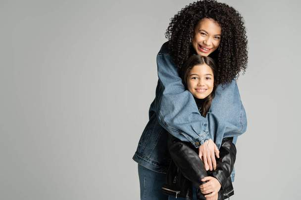 Happy curly mother hugging stylish kid in leather jacket isolated on grey  - Valokuva, kuva