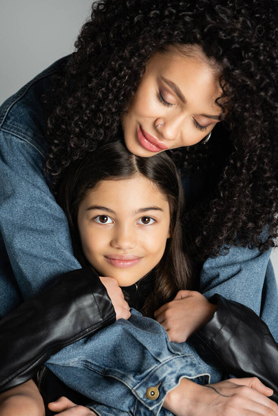 Stylish young woman hugging cheerful preteen daughter isolated on grey  - Photo, Image