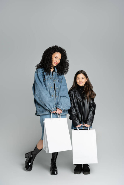 Padres de moda y niña preadolescente sosteniendo bolsas de compras sobre fondo gris  - Foto, Imagen