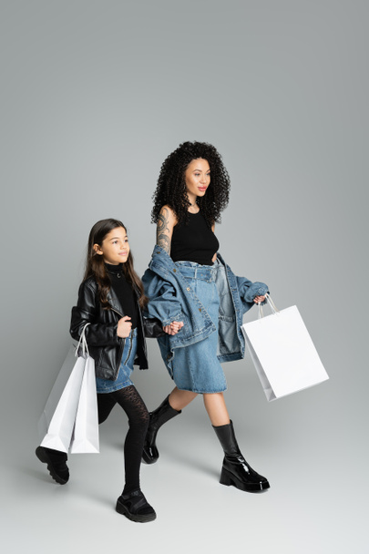 Preteen kid holding shopping bags and hand of stylish mom on grey background  - Foto, Imagem
