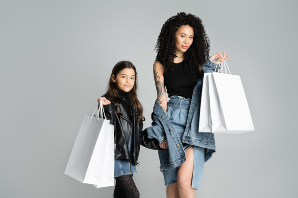 Fashionable mother and child holding purchases on grey background  - Foto, afbeelding