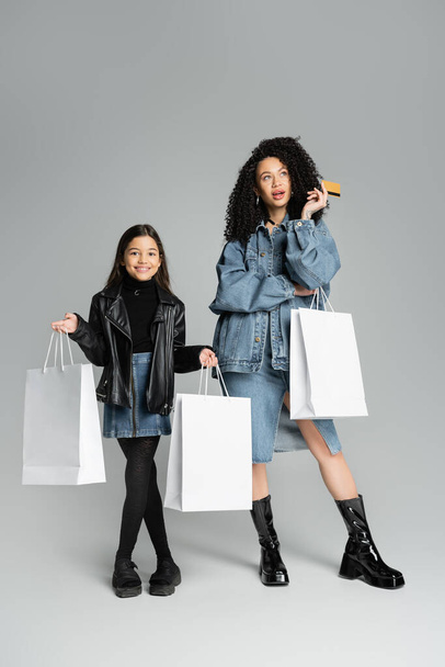 Elegante madre e hija con tarjeta de crédito y bolsas de compras sobre fondo gris  - Foto, Imagen