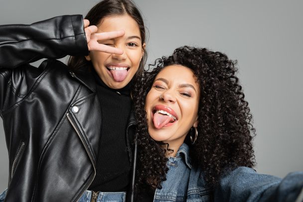 Trendy woman and daughter sticking out tongues isolated on grey  - Photo, Image