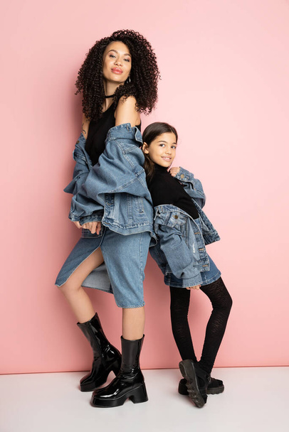 Full length of stylish mom and daughter in denim jackets on pink background  - Foto, Bild