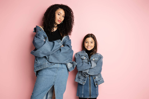 Fashionable woman and kid in denim jackets crossing arms on pink background  - Photo, Image