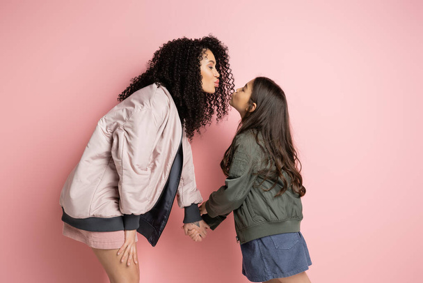 Вид збоку на стильну жінку та дитину, що гладить губи на рожевому фоні
  - Фото, зображення