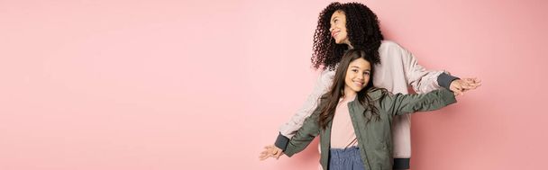 Stylish young woman holding hands of daughter on pink background, banner  - Foto, imagen
