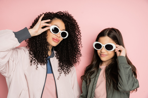 Stylish mother and daughter holding sunglasses on pink background  - Foto, Imagem