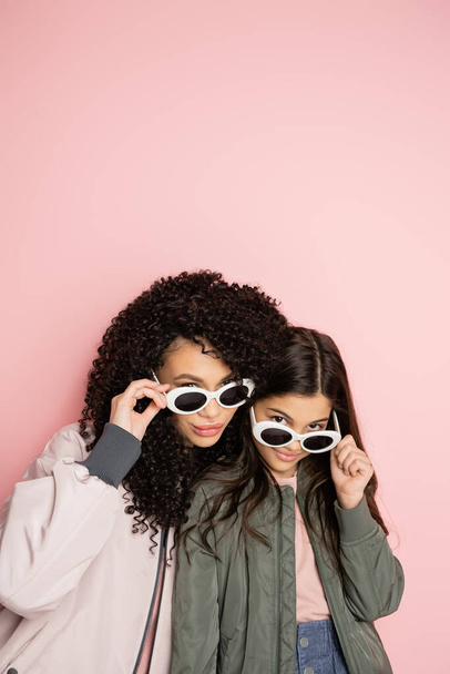 Stylish woman and child in sunglasses looking at camera on pink background  - 写真・画像
