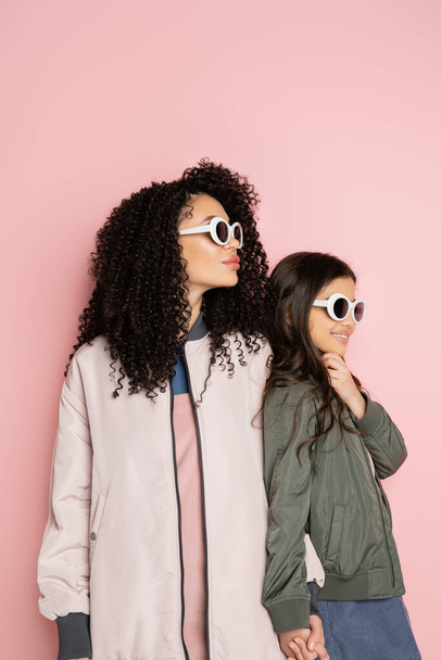 Trendy žena a dívka v slunečních brýlích a bombardér bundy na růžovém pozadí  - Fotografie, Obrázek